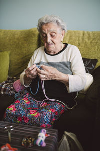 Portrait of crocheting senior woman sitting on couch at home