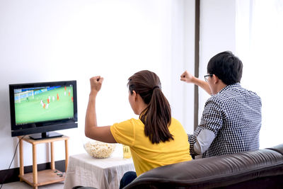 Rear view of friends watching sports on tv while sitting at home