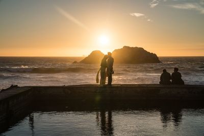 Romantic couple standing on pier at sea shore against sky during sunset