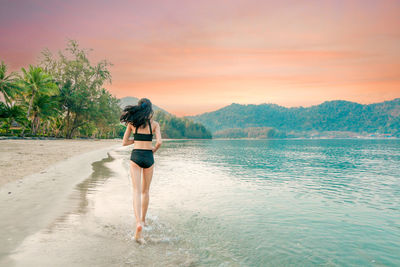 Rear view of woman standing in sea against sky during sunset