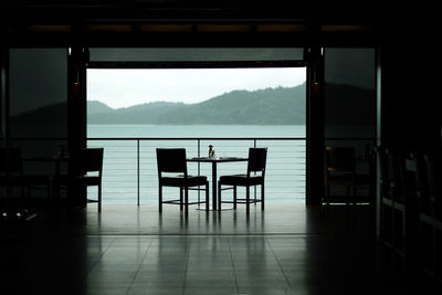 Empty chairs and tables against sky seen through window