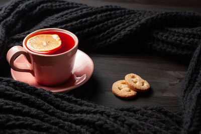 Pink cup of pomegranate tea with lemon, some cookies and knitted scarf on black wooden background