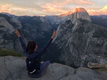 Rear view of woman sitting with arms raised on rock by yosemite national park at morning