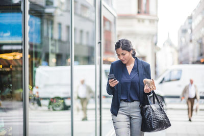 Businesswoman using phone while walking by building