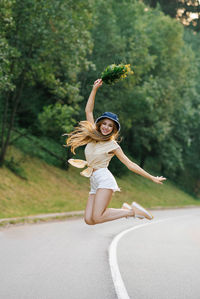 A happy girl in white shorts and a yellow blouse jumps up with a bouquet of flowers, standing 