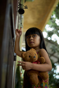 Low angle view of girl holding teddy bear standing at entrance