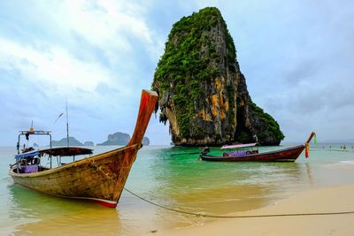 Longtail boats moored on shore at beach against sky