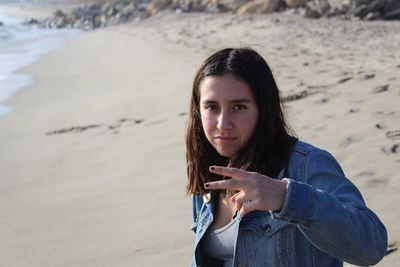 Portrait of young woman gesturing peace sign while standing at beach