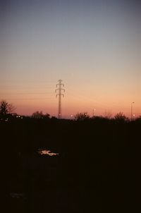 Silhouette of electricity pylon on field against sky at sunset