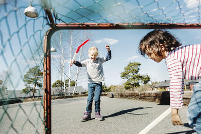 Excited girl gesturing while playing hockey with boy at yard