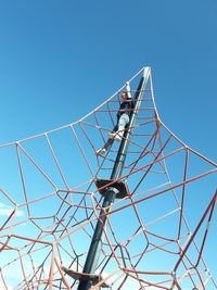 Low angle view of woman on metallic structure against clear blue sky
