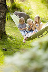 Three girls sitting in hammock holding young chickens