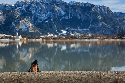 Man sitting on rock by lake against mountains