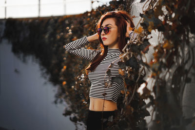 Young woman wearing sunglasses while standing by wall