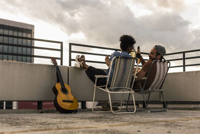 Young couple with beer and guitar sitting on rooftop