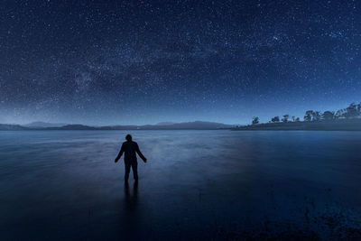 Rear view of man standing on land against sky at night