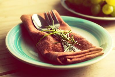 Close-up of silverware with napkin and rosemary in plate on table