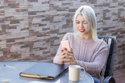 Young woman using phone while sitting at table