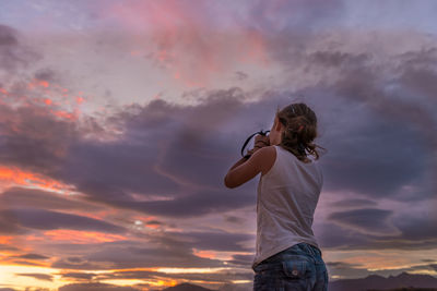 Rear view of woman standing against sky during sunset