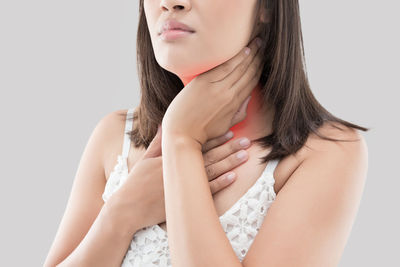 Midsection of woman having neck pain against white background