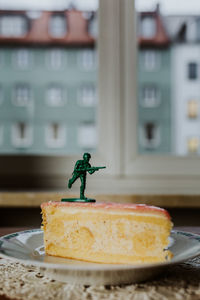 Toy soldier standing on the top of a piece of cake - close up of figurine against window background