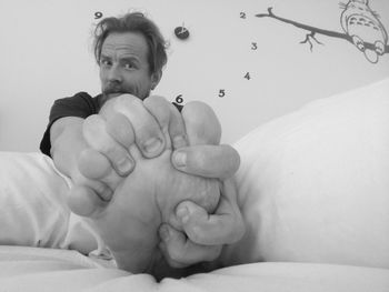 Portrait of mature man holding leg while relaxing on bed at home