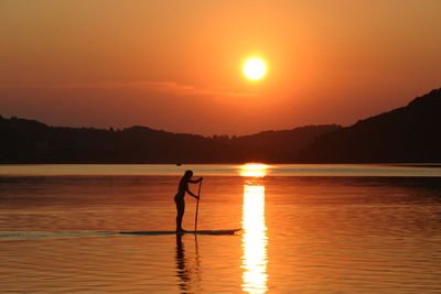 Silhouette woman in lake against orange sky