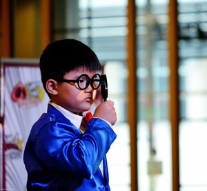 Side view of boy in blue suit holding magnifying glass