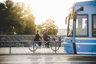 Full length side view of senior couple riding tandem bike on bridge