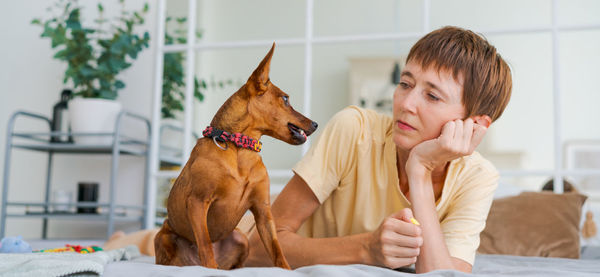 Mature woman lies on floor with slittle dog miniature pinscher, enjoying