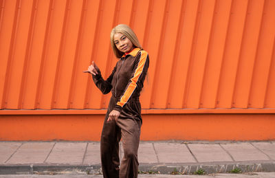 Cheerful african american woman in sportswear dancing in the street on an orange background