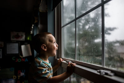 Excited boy looking out a window with raindrops at a stormy sky