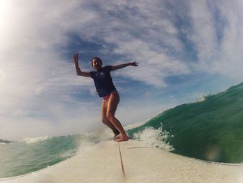 Full length of young woman surfing on sea against sky