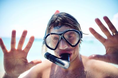 Close-up portrait of mid adult man wearing snorkel mask standing at beach against sky