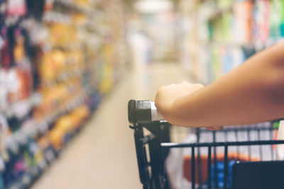 Cropped hand of woman holding shopping trolley in supermarket