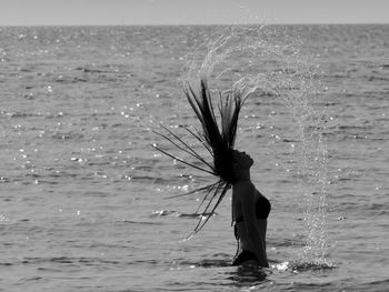 Woman tossing hair in sea against sky