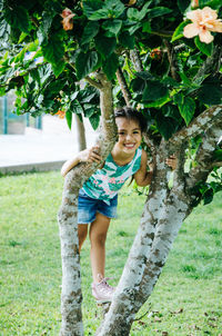 Portrait of girl smiling while standing on tree at park