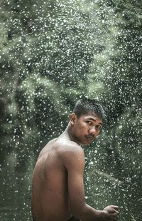 Portrait of shirtless man standing against defocused background during rainy season