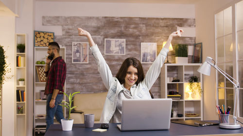 Happy woman with arms raised looking at laptop