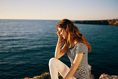 Beautiful woman sitting by sea against sky