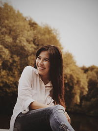 Portrait of smiling young woman sitting against trees