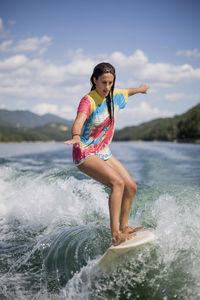 Full length of girl splashing water in sea against sky