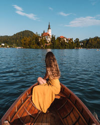 Rear view of woman sitting on lake against sky