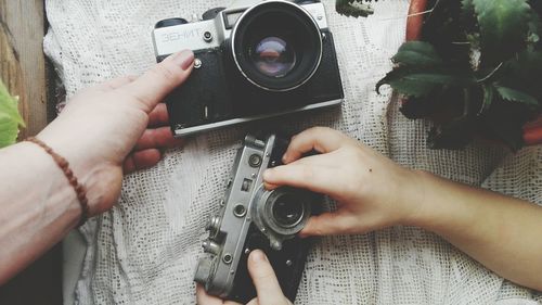 Cropped hands holding cameras at table