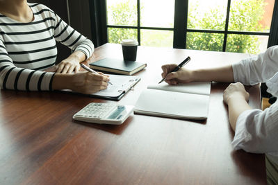 Midsection of woman using smart phone while sitting on table