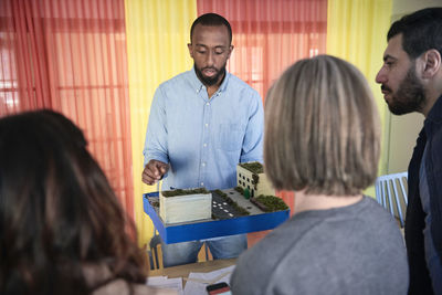 Male engineer explaining colleagues over architectural model during meeting in office