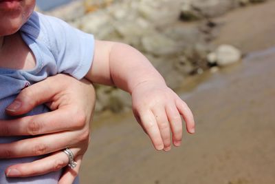 Cropped hand of mother carrying son at beach