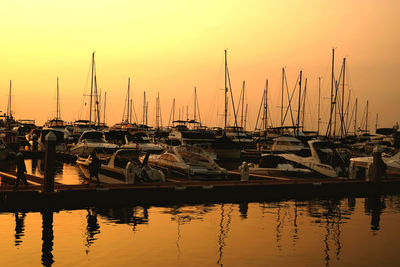 Sailboats moored at harbor during sunset