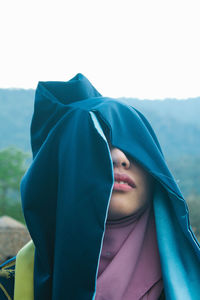 Beautiful young woman with covered face standing against sky outdoors