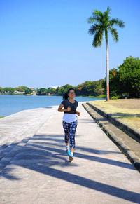 Full length of woman jogging on footpath by lake against sky